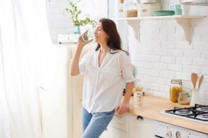 A woman drinks water in her kitchen after eating, following the advice of 21st Century Dentistry, a dentist in Nashville.
